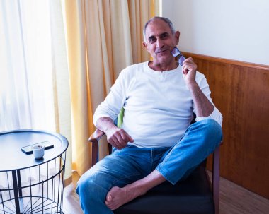 Sessiz, aydınlık bir odada elinde okuma gözlüğü olan olgun bir adam. İfadesi odaklanmış, ortam sıcak ve sade..