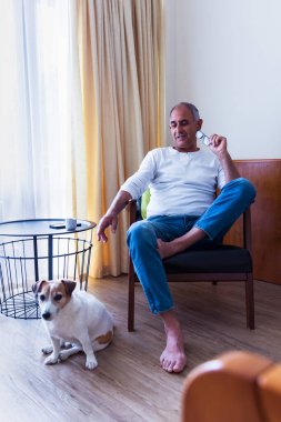 Yaşlı Türk adam odada oturuyor ve küçük köpek Jack Russell terrier ile top oynuyor