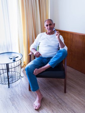 Rahat bir evde tek başına oturan olgun bir adam okuma gözlüğü tutarken dalgın dalgın bakıyor. Bir akıllı telefon ve kahve fincanı yanındaki küçük masada dinleniyor. Sakin ve içsel yaşam tarzı anı.