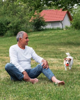 Yaşlı adam bahçede hareketli ve hayat dolu Jack Russell 'ı ile etkileşime geçmeye devam ediyor. Köpek onlar topla oynarken enerjiyle zıplıyor ve havlıyor. Sağlıklı yaşlılara odaklan..