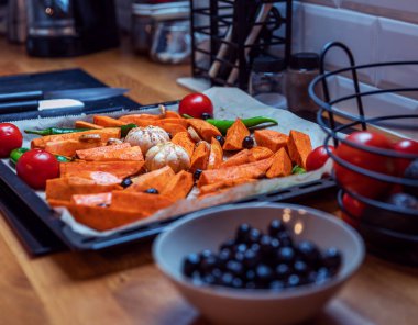 Evde sağlıklı ve basit bir yemek için hazırlanmış rengarenk fırınlanmış sebzelerle dolu tepsi. Tatlı patates, sarımsak, domates, zeytin, yeşil biber ve zencefil besin bakımından zengin bir diyeti yansıtır. Kopyalamak için alanı olan yatay biçim.
