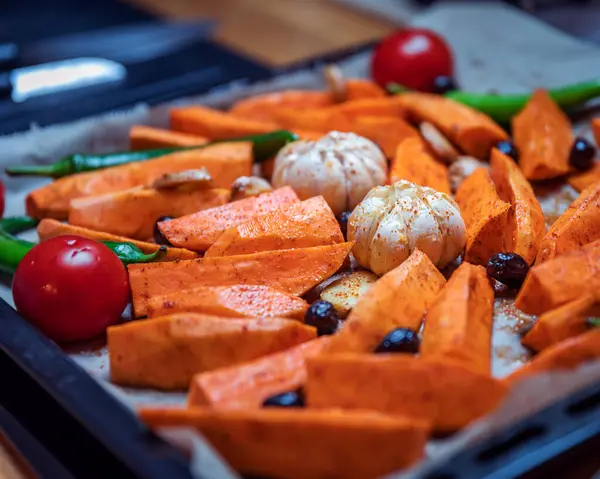 Siyah tepside kızartılmış vejetaryen sebzelerin yakın çekimi: tatlı patates, vişneli domates, zeytin, sarımsak, yeşil biber ve zencefil. Temiz, bitkisel yemek konsepti, yemek ve yaşam tarzı içeriği için ideal. Üstüste gelen metin için görsel kopyalama alanı içerir.