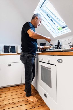 Parlak, modern bir tavan arası mutfağında taze pişmiş yemekleri tek başına servis eden yaşlı bir adam. Sahne bir pencereden gün ışığıyla aydınlatılır. Sağlıklı beslenme, kişisel bakım ve ihtiyarlık dönemindeki dikkatli beslenme temalarını yansıtıyor. A