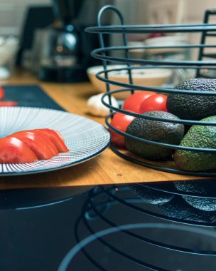 İçinde olgun domatesler, avokado ve sarımsak karanfilleri olan bir sepetin yanında dilimlenmiş taze domateslerle dolu bir tabağın yakın çekimi. İmajda sağlıklı beslenme, vejetaryen yaşam tarzı ve besleyici yemekler ve temiz yemekler için ideal taze organik sebzeler yer alıyor.