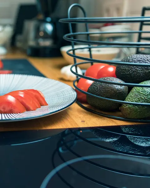 İçinde olgun domatesler, avokado ve sarımsak karanfilleri olan bir sepetin yanında dilimlenmiş taze domateslerle dolu bir tabağın yakın çekimi. İmajda sağlıklı beslenme, vejetaryen yaşam tarzı ve besleyici yemekler ve temiz yemekler için ideal taze organik sebzeler yer alıyor.