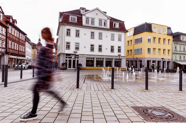 Coburg Bavyera 'da Albertplatz' dan geçen genç bir kadın tarihi Avrupa binaları ve güneşli şehir meydanı atmosferini gösteriyor.