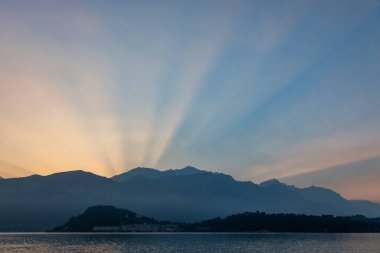 blue hour before sunrise on lake como with sunbeams shining through mountain valleys