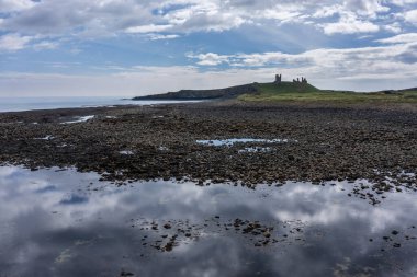 Kuzeyden Dunstanburgh Şatosu alçak gelgitte yükseldi gündüz mavi gökyüzü ve bulutlar 