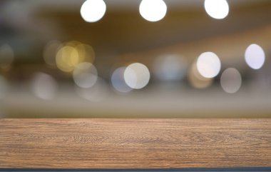 Kafenin soyut bulanık arka planının önündeki boş ahşap masa. Öndeki ahşap tablo ürünlerinizi görüntülemek veya montajlamak için kullanılabilir. Produc gösterimi için modelleyin