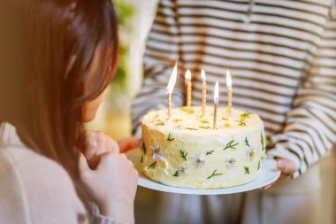 Cheerful friends enjoying home Birthday holiday party. Asian sister cheering drinking red wine celebrating with Birthday cake