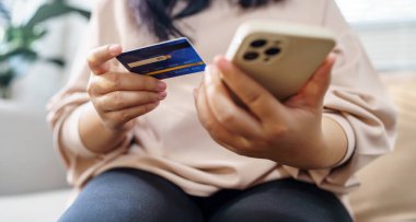Online alışveriş için akıllı telefonu olan yaşlı bir kadın. Elinde cep telefonu var. Kredi kartıyla ödeme yapıyor.