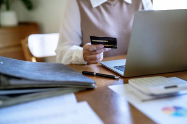 Bilgisayarda alışveriş yapan bir kadın internet üzerinden elektronik alışveriş için kredi kartı tutuyor. İnternet üzerinden alışveriş yapıyor. Online alışveriş cep telefonu laptop teknolojisi. 