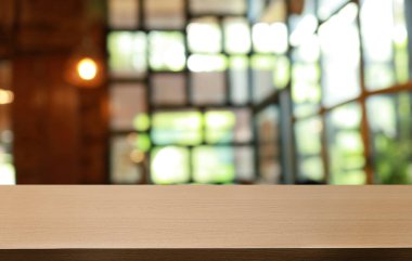 Kafenin soyut bulanık arka planının önündeki boş ahşap masa. Öndeki ahşap tablo ürünlerinizi görüntülemek veya montajlamak için kullanılabilir. Produc gösterimi için modelleyin