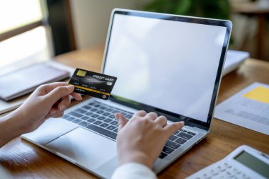 Bilgisayarda alışveriş yapan bir kadın internet üzerinden elektronik alışveriş için kredi kartı tutuyor. İnternet üzerinden alışveriş yapıyor. Online alışveriş cep telefonu laptop teknolojisi. 