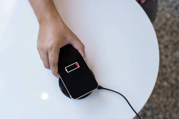 Charging mobile phone battery with wireless charging device in the table. Smartphone charging on a charging pad. Mobile phone near wireless charger Modern lifestyle technology concept