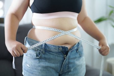 Diyet konseptinde şişman göbekli obez kadın. Kilolu bir kadın şişman karnına dokunuyor ve kilo vermek istiyor. Şişman kadının belinde bir santimetre var.