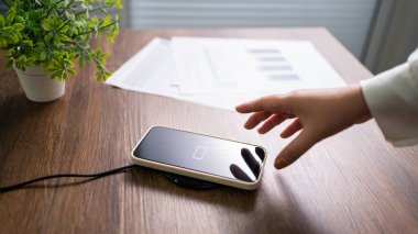 Masada kablosuz şarj cihazıyla cep telefonu bataryası şarj ediliyor. Akıllı telefon şarj cihazına yükleniyor. Kablosuz şarj cihazının yanındaki cep telefonu Modern yaşam tarzı teknolojisi 