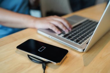 Charging mobile phone battery with wireless charging device in the table. Smartphone charging on a charging pad. Mobile phone near wireless charger Modern lifestyle technology concept.