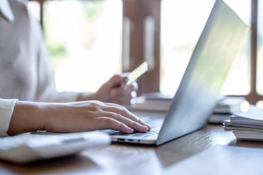 Bilgisayarda alışveriş yapan bir kadın internet üzerinden elektronik alışveriş için kredi kartı tutuyor. İnternet üzerinden alışveriş yapıyor. Online alışveriş cep telefonu laptop teknolojisi. 