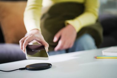 Masada kablosuz şarj cihazıyla cep telefonu bataryası şarj ediliyor. Akıllı telefon şarj cihazına yükleniyor. Cep telefonu kablosuz şarj cihazının yanında..