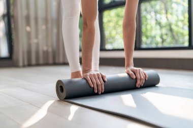 Spor salonundaki kadın yoga stüdyosunda çalışmadan önce spor paspası katlıyor. Sağlıklı yaşam tarzını eğittikten sonra yoga minderi sarmak
