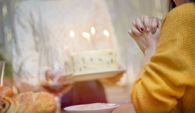 Cheerful friends enjoying home Birthday holiday party. Asian sister cheering drinking red wine celebrating with Birthday cake