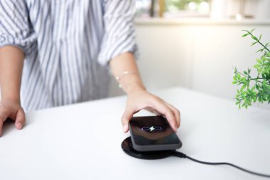 Masada kablosuz şarj cihazıyla cep telefonu bataryası şarj ediliyor. Akıllı telefon şarj cihazına yükleniyor. Cep telefonu kablosuz şarj cihazının yanında.