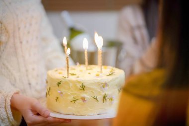 Cheerful friends enjoying home Birthday holiday party. Asian sister cheering drinking red wine celebrating with Birthday cake