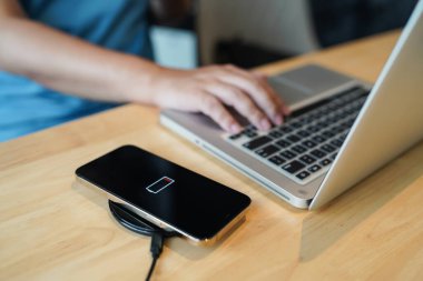 Charging mobile phone battery with wireless charging device in the table. Smartphone charging on a charging pad. Mobile phone near wireless charger Modern lifestyle technology concept.