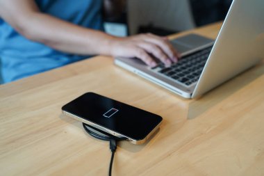 Charging mobile phone battery with wireless charging device in the table. Smartphone charging on a charging pad. Mobile phone near wireless charger Modern lifestyle technology concept.