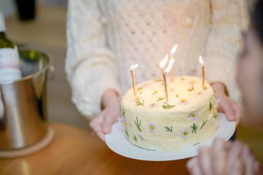 Cheerful friends enjoying home Birthday holiday party. Asian sister cheering drinking red wine celebrating with Birthday cake