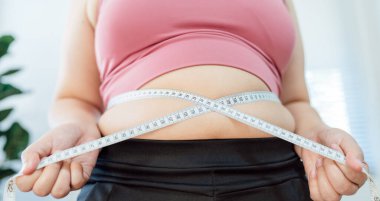 Diyet konseptinde şişman göbekli obez kadın. Kilolu bir kadın şişman karnına dokunuyor ve kilo vermek istiyor. Şişman kadının belinde bir santimetre var.