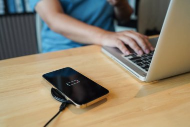 Charging mobile phone battery with wireless charging device in the table. Smartphone charging on a charging pad. Mobile phone near wireless charger Modern lifestyle technology concept.