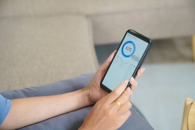Akıllı evi kontrol eden Asyalı kadın. Oturma odasında akıllı ev uygulaması olan cep telefonu. Ekran teknolojisine dokun. Uzak ev denetim sistemi