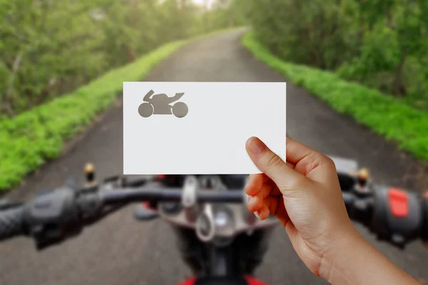 Man\'s hand holding bike symbol paper on road. Concept of journey, travel, dream, freedom. Hand is holding paper bike against road seated on bike with empty space for text.