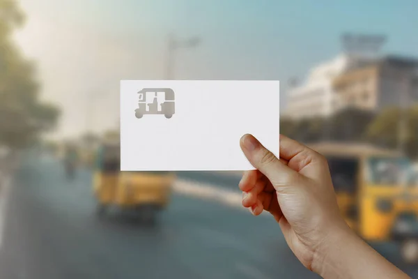 Man\'s hand holding Auto Rickshaw symbol paper on road. Concept of journey, travel, dream, freedom. Hand is holding paper Auto Rickshaw against road with empty space for text.