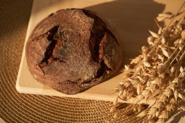 Mayasız bir başlangıç ve tam tahıl, çavdar ve buğday unu karışımı üzerine taze pişmiş çavdar ekmeği manzarası. Kurumuş bir çiçeğin yanında tahtanın üzerinde duruyor. Seçici odak, güneş. Boşluğu kopyala