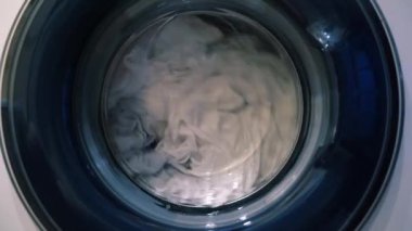 Çamaşır makinesinde kururken çamaşırların hareketi. Çamaşır makinesinin varilinde ıslak şeyler var. Yüksek kalite 4k görüntü