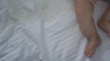 Yeni doğmuş bir bebeğin bacakları mutlu bir şekilde yatağa vuruyor. Çocuk sırtüstü uzanmış yatağa işiyor. Annelik, aile, doğum kavramı. Yüksek kalite 4k görüntü