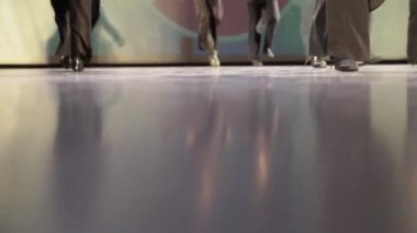 Yerde yansıma var. Uzaktaki kızlar sert zeminde step dansı yapıyorlar. Aşağıdan bir dans sahnesi. Pantolonlu kadın bacakları ve siyah ayakkabılar. Hafif bir tekme. Seçici odaklanma. Yüksek kalite 4k görüntü