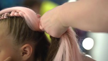 Pembe kanekalonlu bir çocuk için örgü ören ellerin yan görüntüsü. Kanekalon örgüleri örmede usta sınıf konsepti. Yüksek kalite 4k görüntü