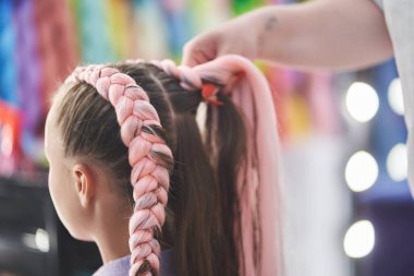 Usta, çocukların saçlarını pembe bir kanekalondan örüyor. Yakın plan, yan görüş. Ustanın elleri saçına kanekalon kumaşı dokudu. Yüksek kalite fotoğraf