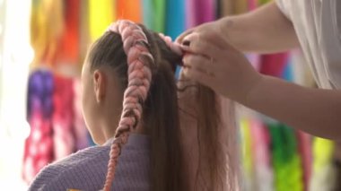 Sarı saçlı, dikiz aynalı bir kız için kanekalon örgüleri örüyorum. Usta, çocukların saçlarını ve ellerini yakın plan örüyor. Yüksek kalite 4k görüntü