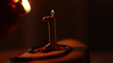 En az detay içeren, ortasında ince bir mum bulunan bir pasta, 1 numara. Bir el mumu yakar ve bir ateş yakar. Yüksek kalite 4k görüntü