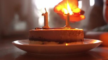 Bir kadın mumları yakar. 11 numaralı doğum günü pastası tabakta. Doğum günü kutlaması. Mumlardaki ateş yanıp sönüyor. Yüksek kalite 4k görüntü