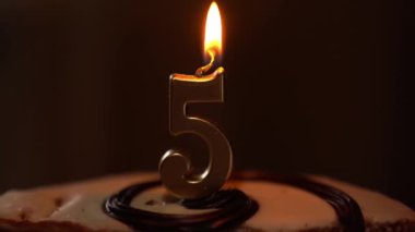 Doğum günü pastasının üzerindeki mumları üfleyerek. 5 numaralı mumla. Alevler mumun üzerinde yanıp sönüyor. Doğum günü kutlaması geleneği. Yüksek kalite 4k görüntü