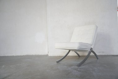 Metal bacaklı beyaz deri bir koltuk beton bir duvarın arka planında boş bir odada duruyor. Kopyalayacak yer de var. Yüksek kalite fotoğraf