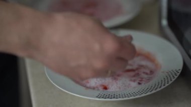 Bir erkeğin eli çilekli püreyi bir kaşıkla bir tabakta sütle karıştırır. Tabakta kırmızı çilek ezmesi. Evde tatlı var. Bir çocuğun eli tabağa uzanır. Yüksek kalite 4k görüntü