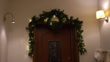 Bir sürü beyaz ışığı olan bir Noel ağacı dalı, telin üzerindeki bir LED çelenk ön kapıyı süslüyor. Yaklaşan Noel 'in sembolü olarak şenlik dekorasyonları. Yüksek kalite 4k görüntü