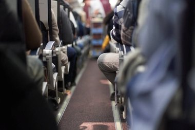 Koltuklarında yolcular oturan bir uçağın içi. Erkek bir kâhya yemek dağıtıyor. Yolcular uçakta sıra boyunca otururlar. Seyahat kavramı. Yüksek kalite fotoğraf